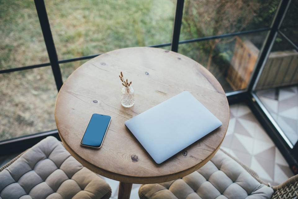 Laptop dan smartphone di meja kayu bundar di interior yang nyaman.